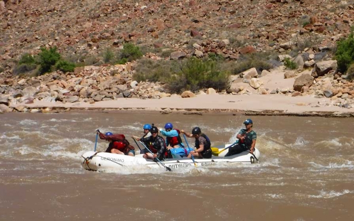 A group of students paddle a raft on choppy water